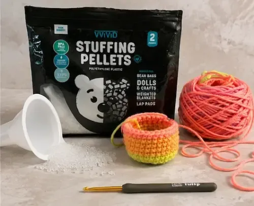 Poly stuffing beads beside a crochet hacky sack, yarn, funnel, and crochet hook